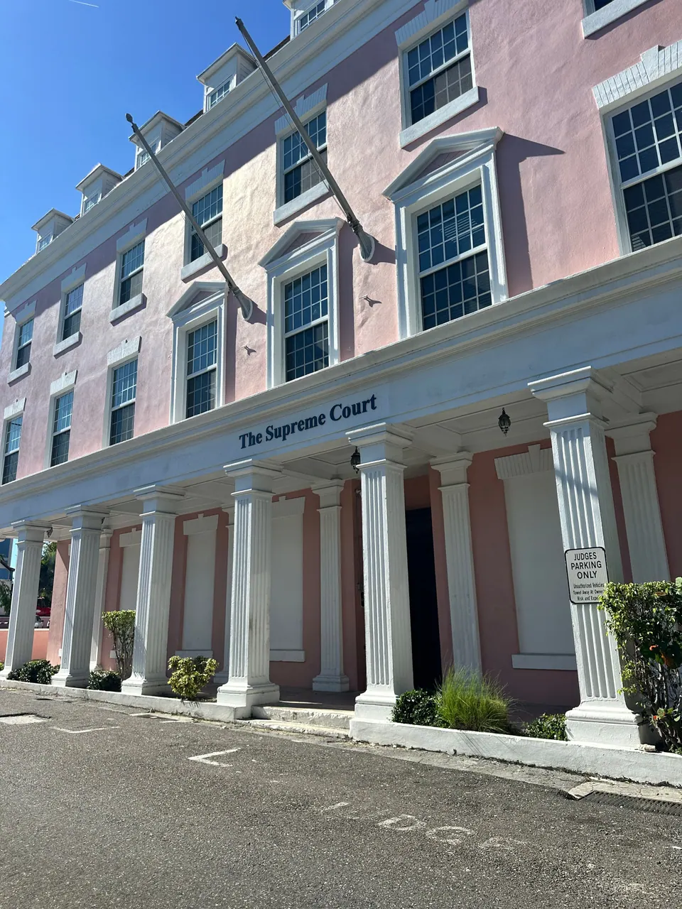A pink two-storey colonial building with a white colonnade carries a sign reading The Supreme Court, with a no-parking notice on the pillar beside it.