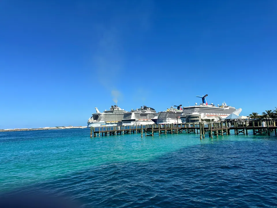 Several large cruise ships are lined up at a long pier across clear turquoise water under a deep blue sky.