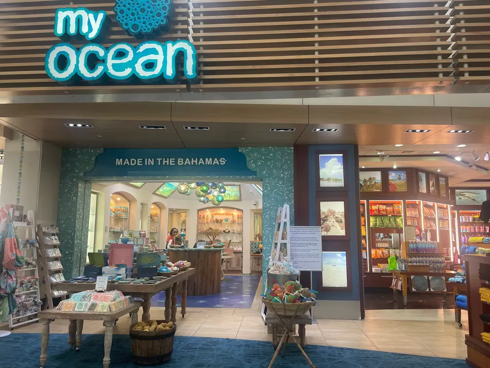 A gift shop in an airport concourse with a Made in the Bahamas banner over the doorway and souvenir tables in front.