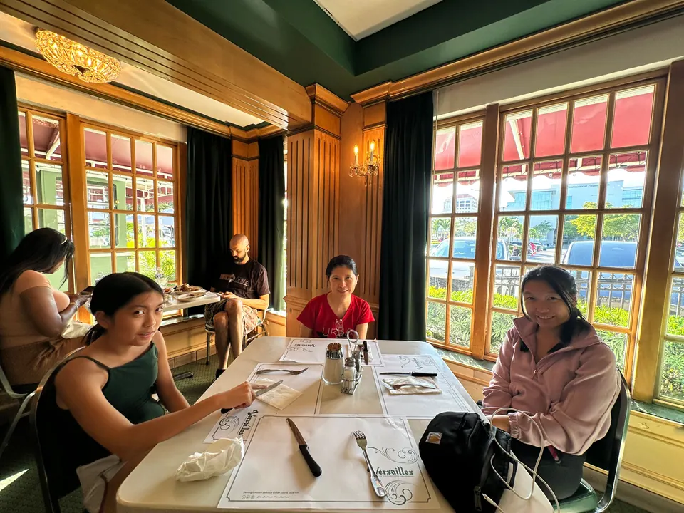 People sit around a white-clothed table with paper placemats in a wood-panelled restaurant with tall windows and dark green curtains.