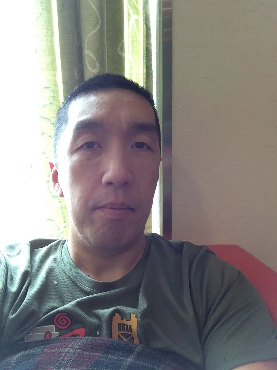 A close selfie of a man in a gray T-shirt sitting by a bright window in a ship corridor.