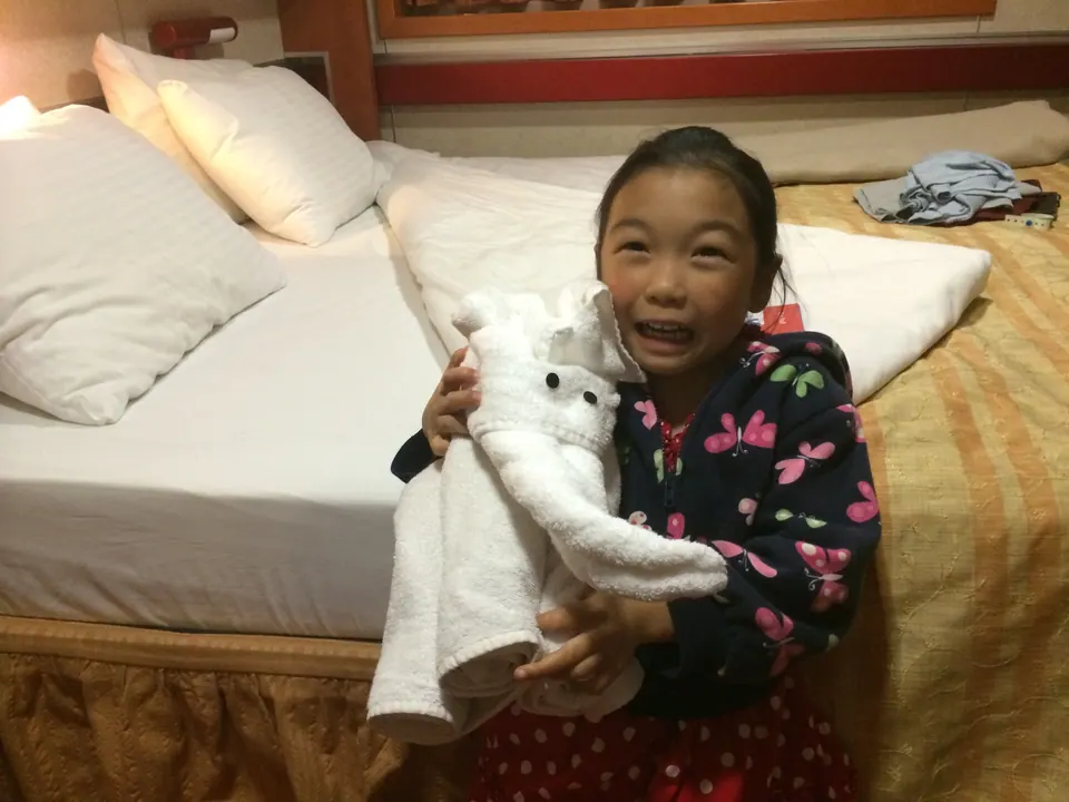 A girl in a butterfly-print jacket holds a folded towel elephant close and grins at the camera.