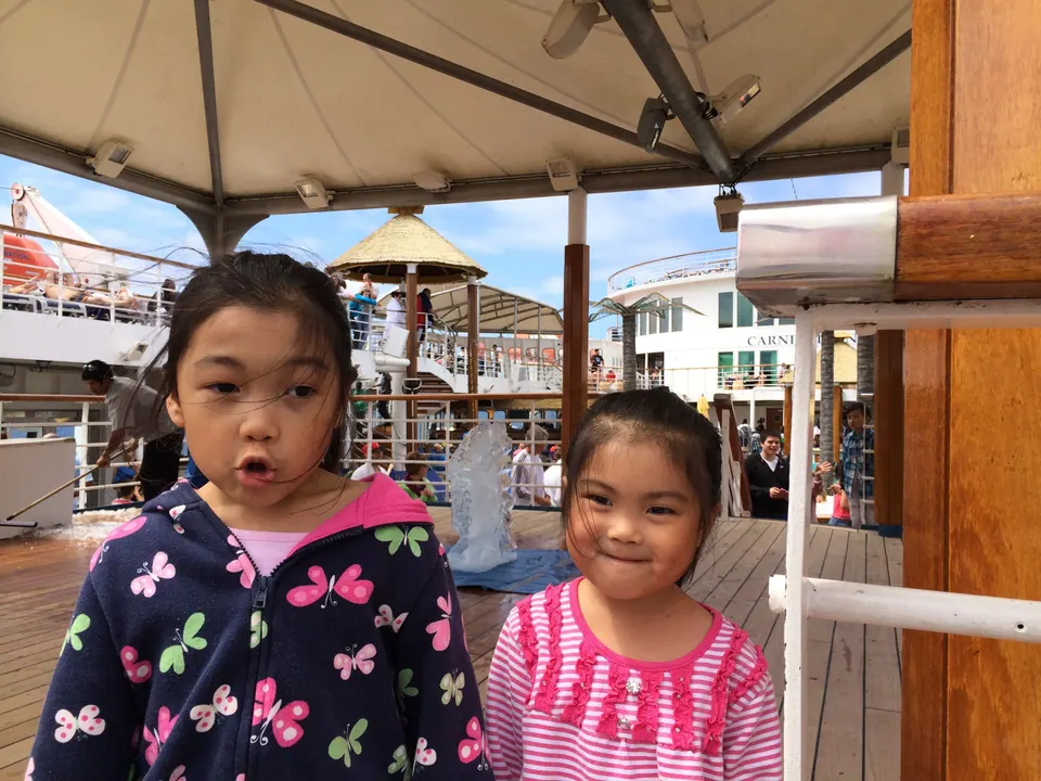 Two small girls make a funny face and a smile under the canopy, with a glinting ice carving on the deck behind them.