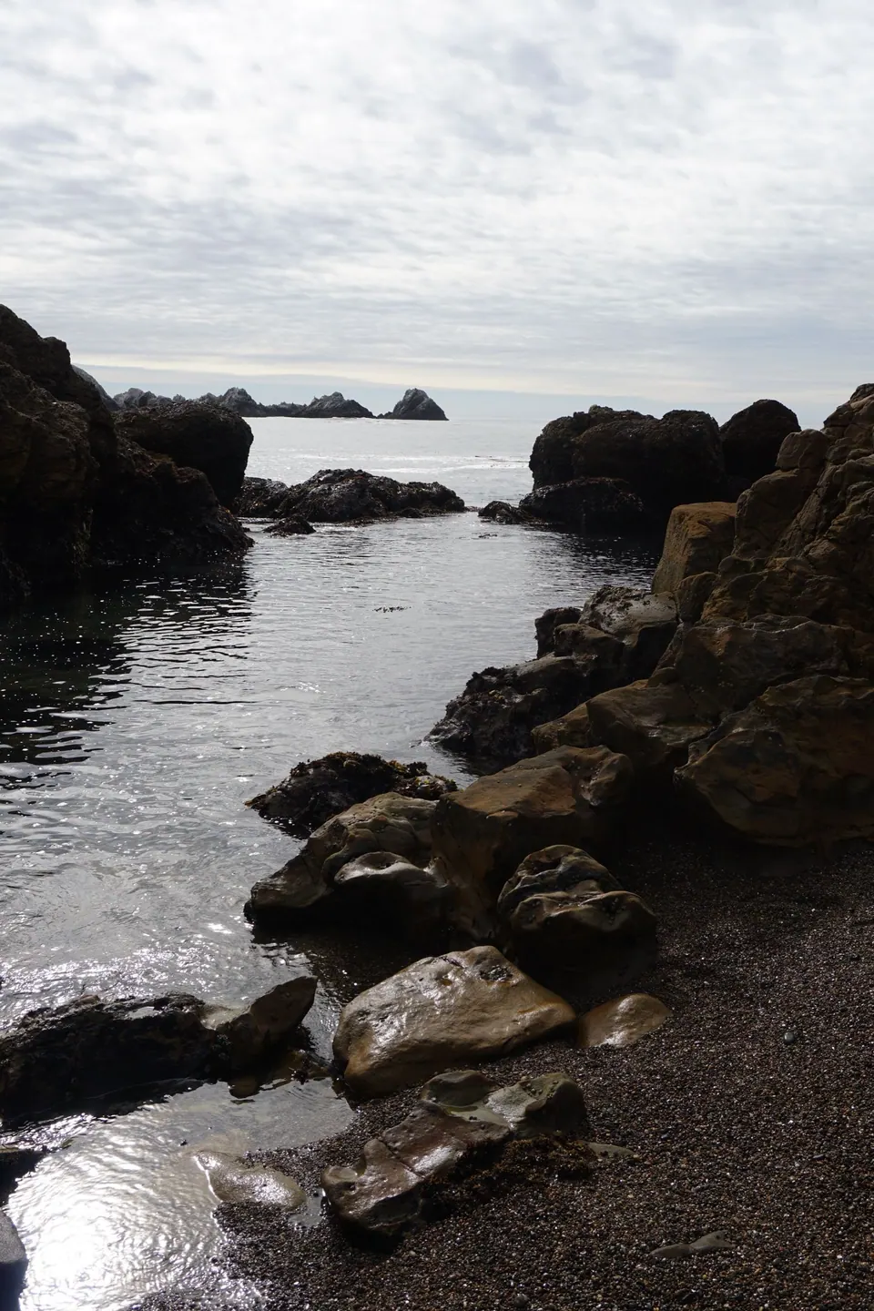 A calm tide channel between dark rocks with sea stacks in the distance.