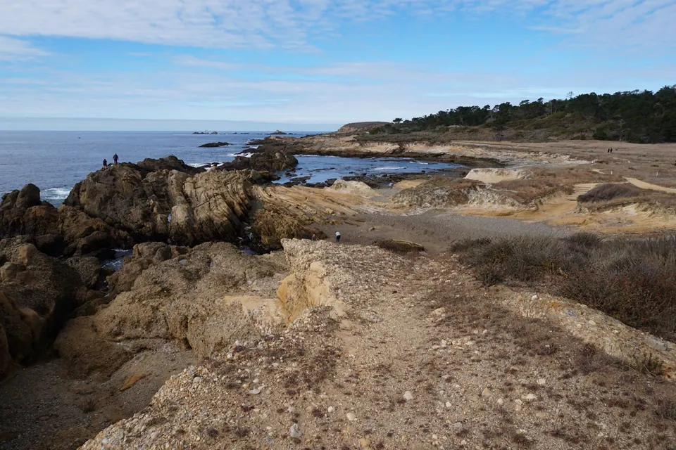A layered sandstone headland with a blue tide pool and the sea beyond under scattered clouds.