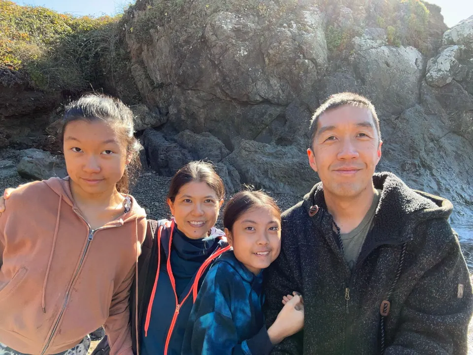 A man, two girls and a woman crowd into a selfie in front of a rocky bank with sun flare across the top.