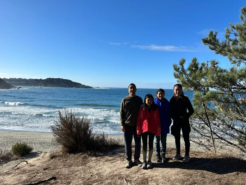 A tall man, a girl in red, a woman in blue and a girl in a gray fleece stand in a row on the bluff above the sea.