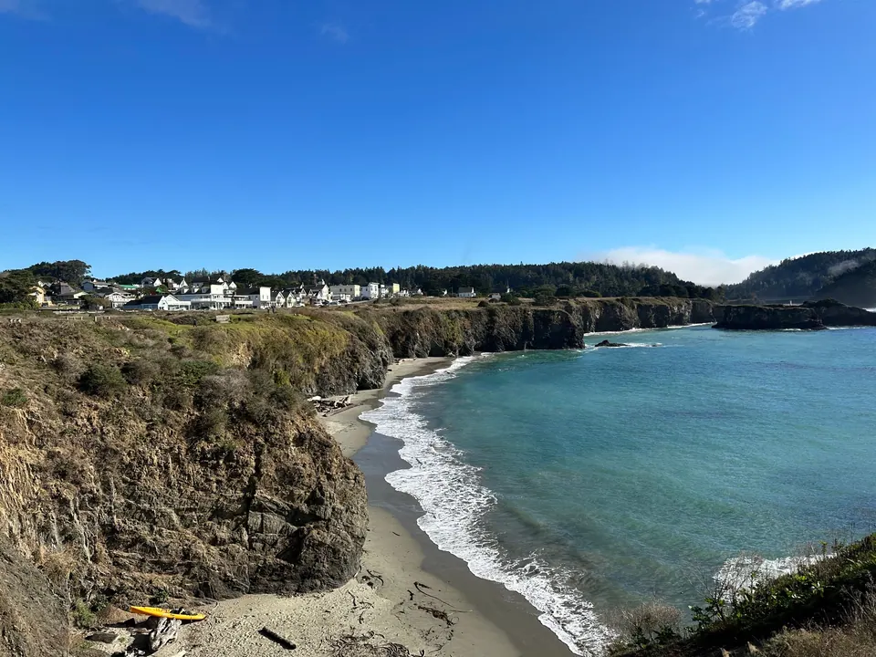 A curved beach in a green cove below dry headlands, with village houses along the far bluff.