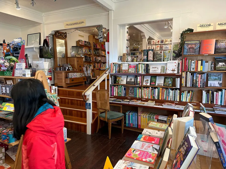 A girl in a red jacket browses shelves in a crowded shop full of books and cards.