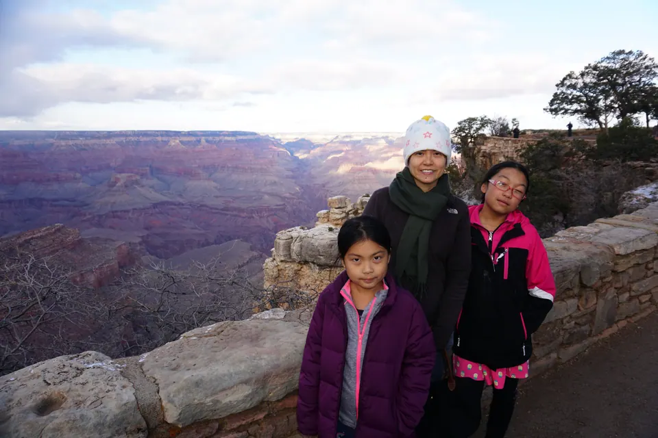 A woman and two girls stand at a stone wall, the canyon's purple and red layers stretching away behind them.