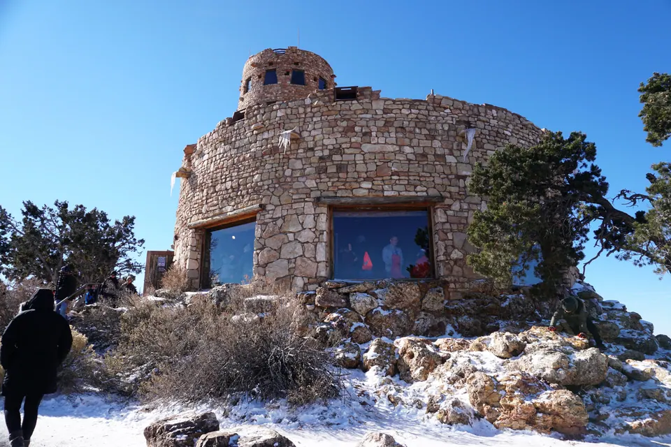 A round stone building with big windows and a small turret on top, snow and icicles along its walls, under a clear blue sky.