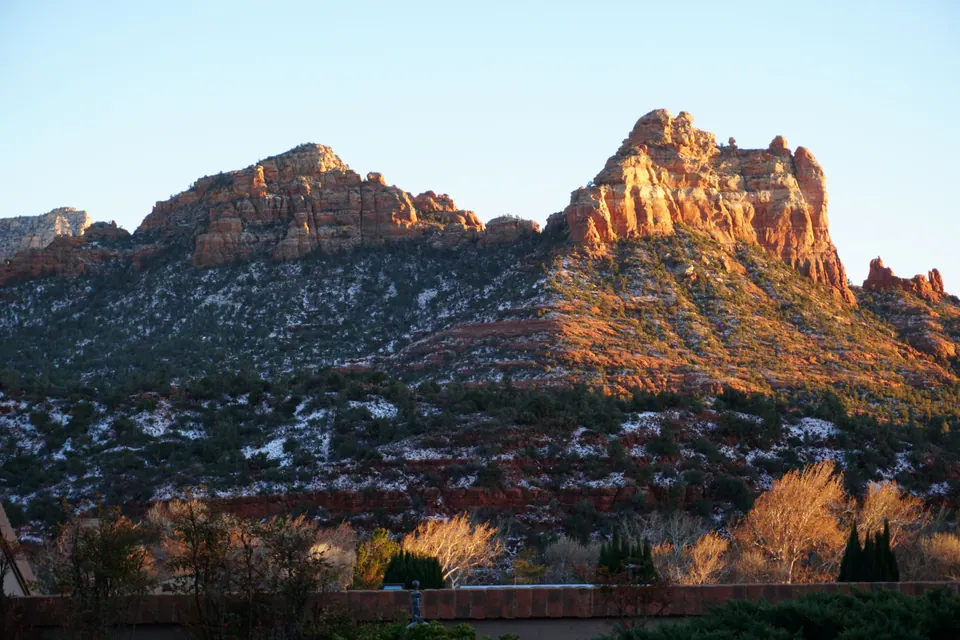 Red-rock peaks glow orange in low sun above snowy slopes and bare cottonwoods.