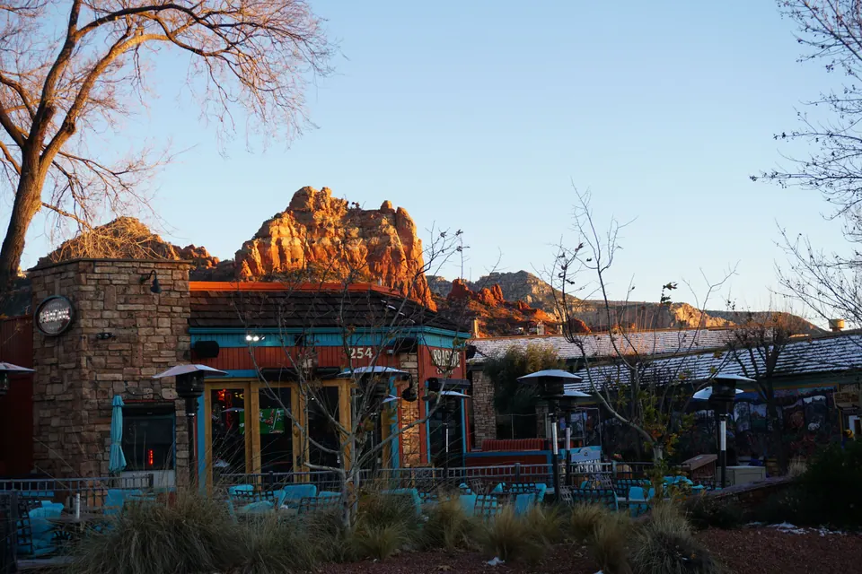 A stone-and-timber restaurant with turquoise patio chairs and heaters, the red rocks lit by the last sun behind it.