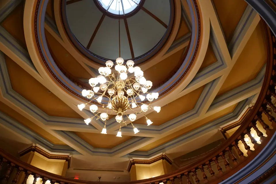 A brass chandelier of glass globes hangs from a skylit dome ringed by a wooden balcony.