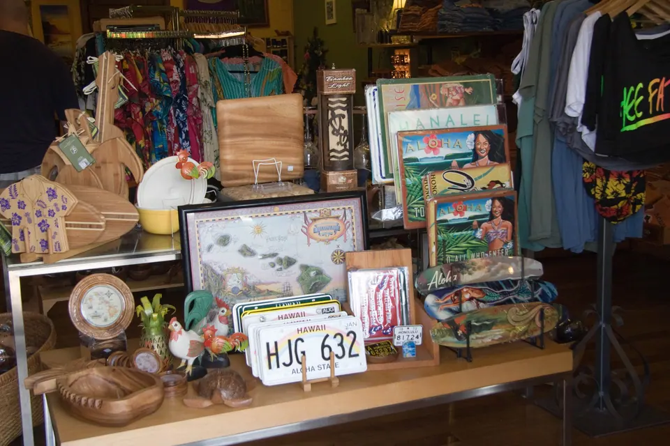 A table of Hawaiian souvenirs in a gift shop: carved wooden pieces, a map of the islands, aloha shirts and a Hawaii license-plate novelty.