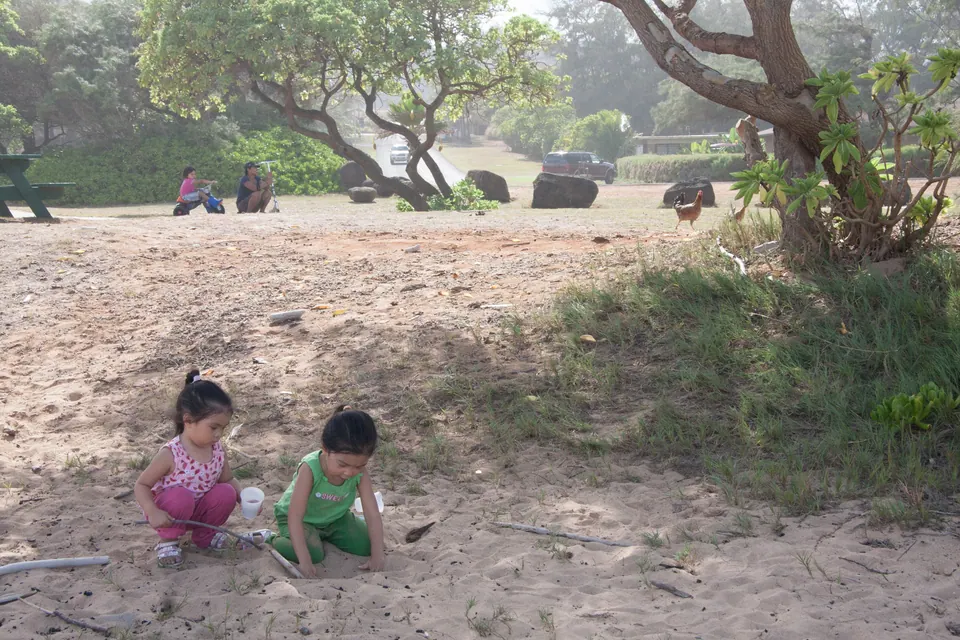 A close view of two small girls in pink and green squatting side by side in the sand.