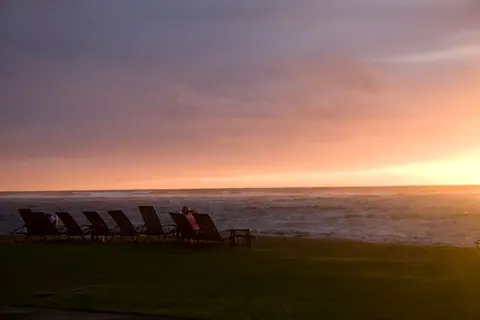 A warm orange sunrise over the horizon with a line of lounge chairs and a person seated at the far end.