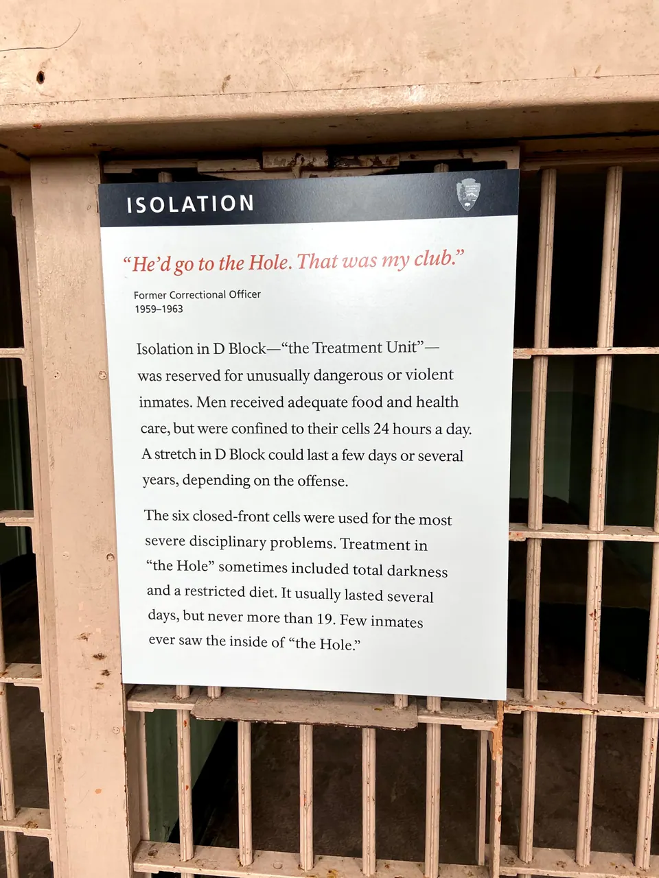 A National Park Service panel titled Isolation hangs on the bars of a cell, with a quotation from a former officer about the Hole.