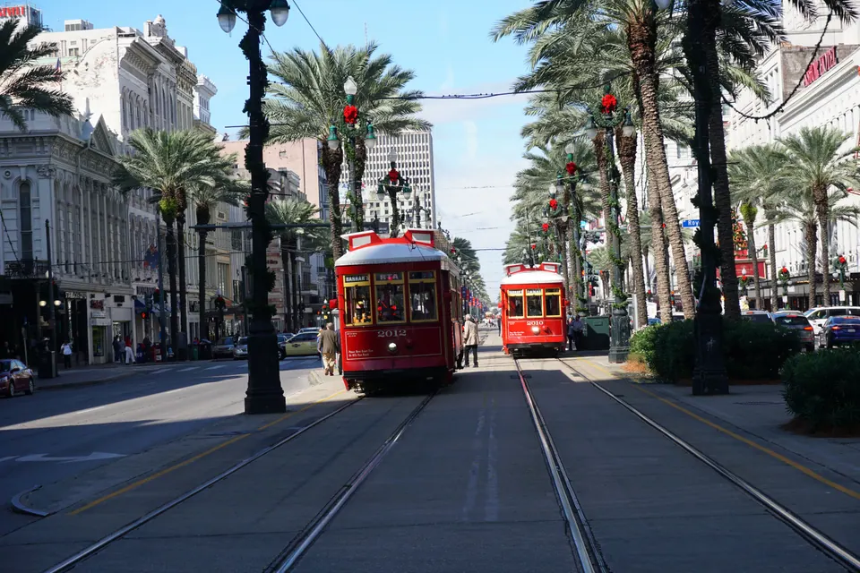 Two red streetcars come down the palm-lined middle of Canal Street on a sunny morning, the palms wrapped in holiday garlands.