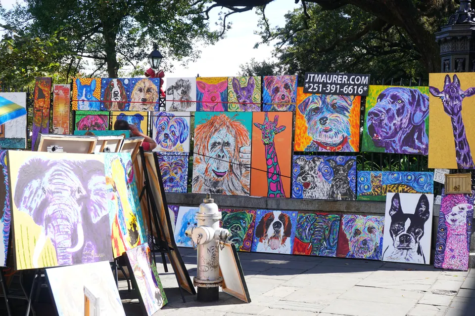 Brightly colored paintings of dogs, giraffes and an elephant hang on an iron fence and stand on easels on the flagstones.