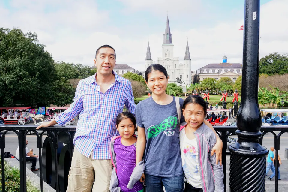 A man, a woman and two girls stand at a black iron railing, with Jackson Square and the cathedral's spires behind them.