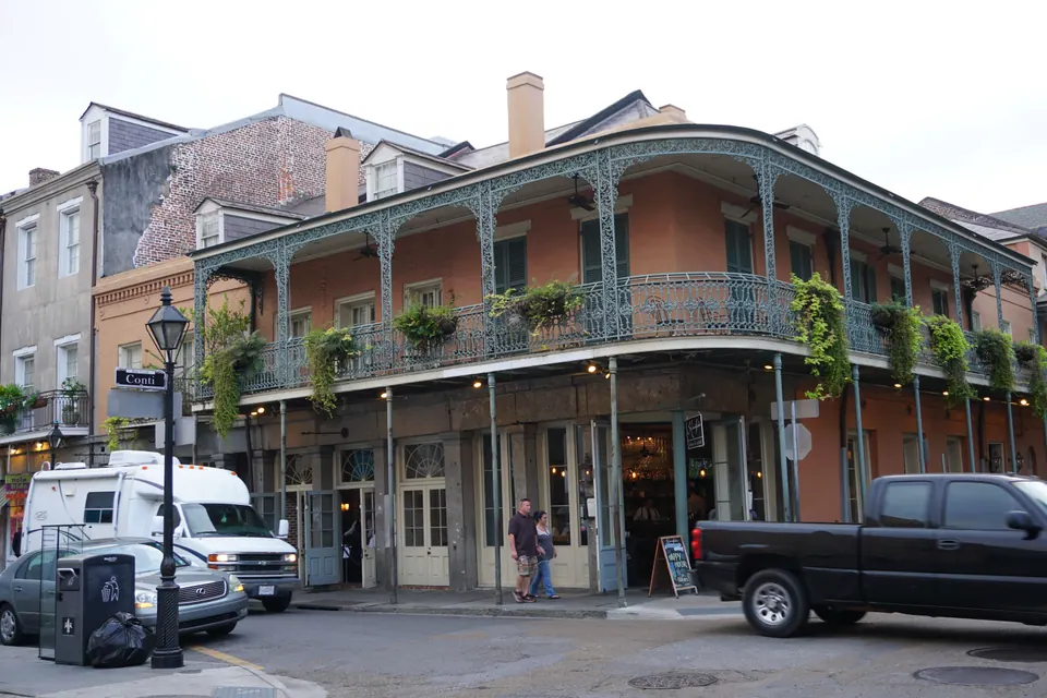 A salmon-colored building with a long lacy iron gallery hung with ferns at a French Quarter street corner.