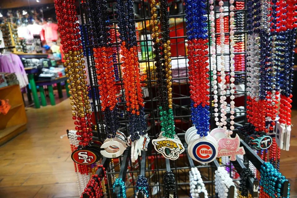 Racks of Mardi Gras bead necklaces with sports-team medallions in a souvenir shop.