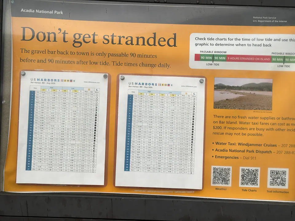 A yellow Acadia National Park sign headed Don't get stranded, with two posted tide tables, warns that the gravel bar back to town is passable only 90 minutes before and after low tide.
