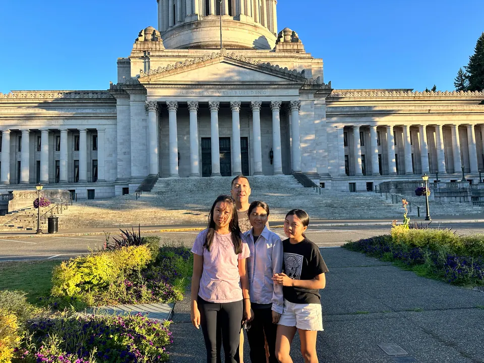Three people stand in front of the columned Washington State Capitol in warm evening light.