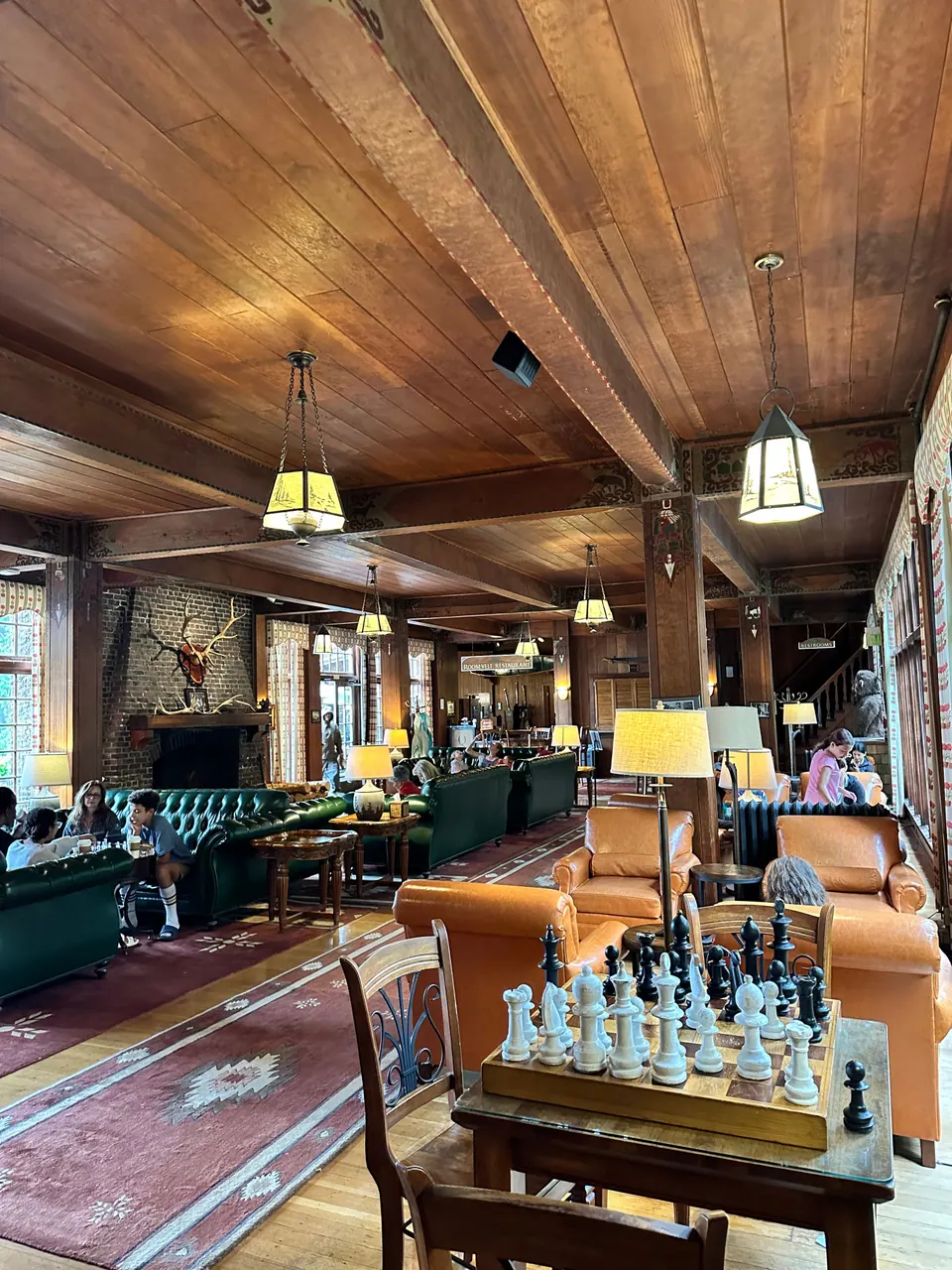A wood-paneled lodge room with leather armchairs, hanging lamps and a chess board in the foreground.