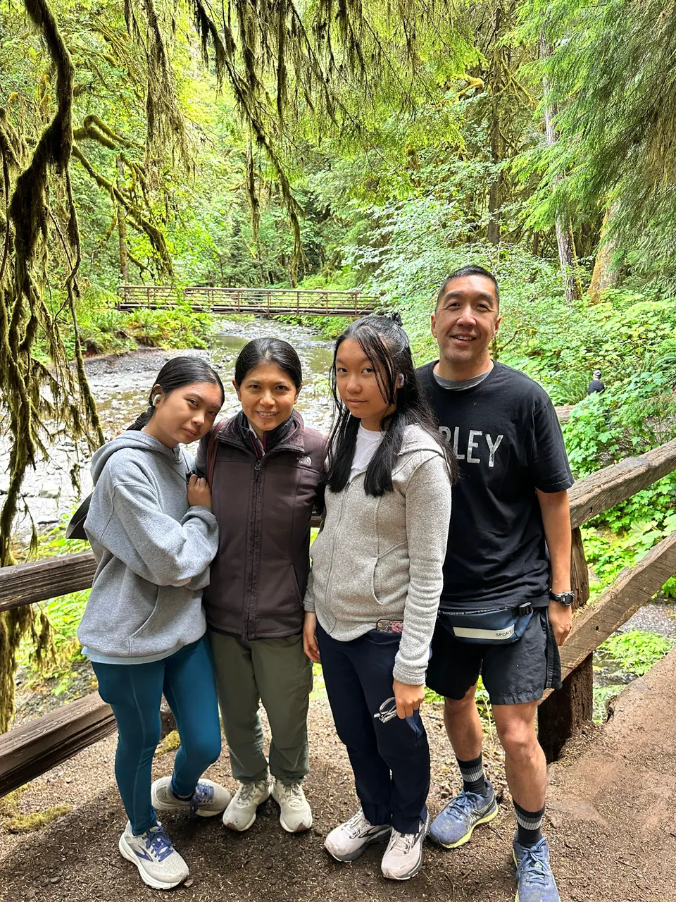 Four people stand together on a wooden footbridge in a mossy forest.