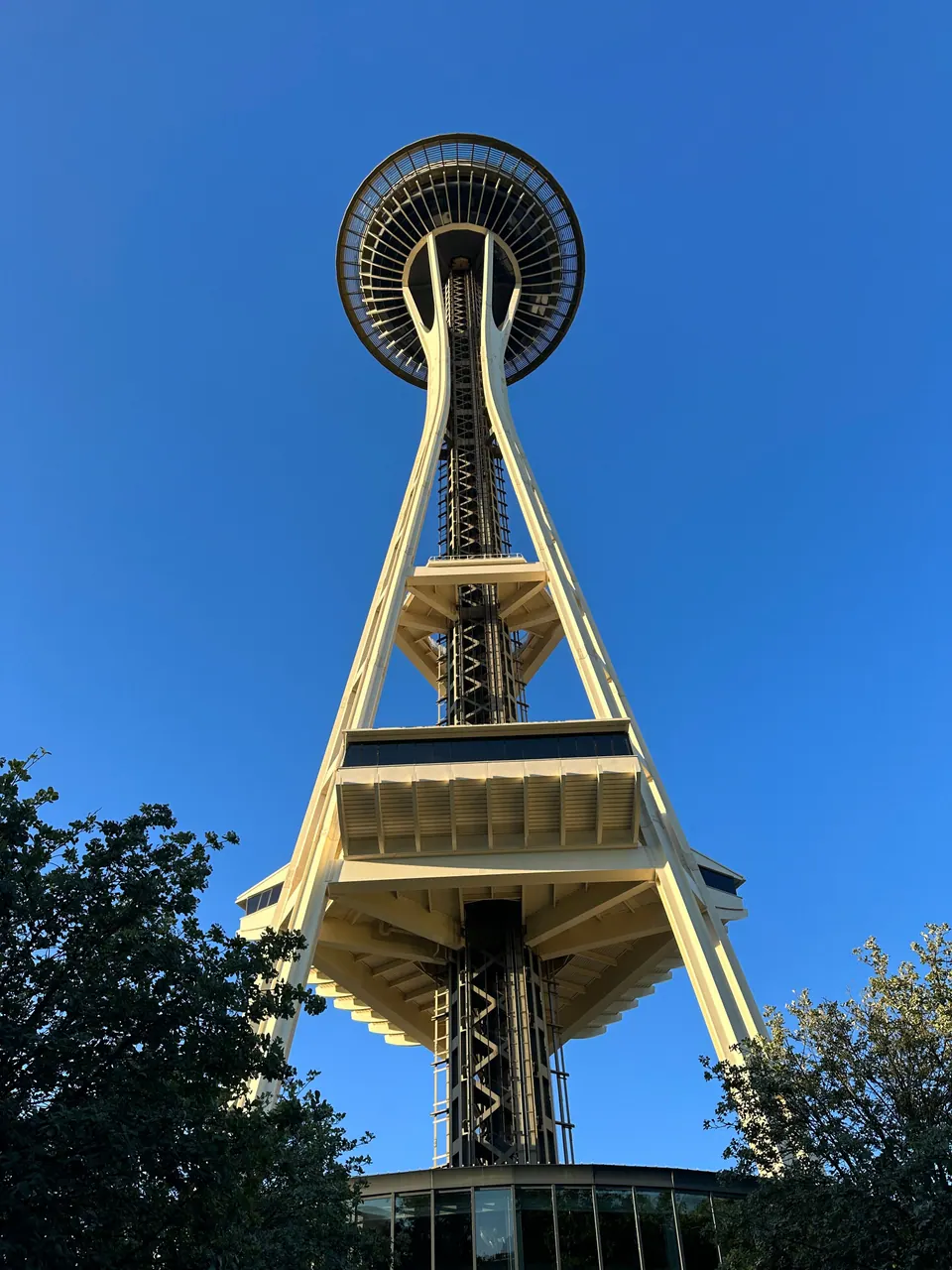 Looking straight up at the Space Needle's legs and saucer-shaped top against a deep blue sky.