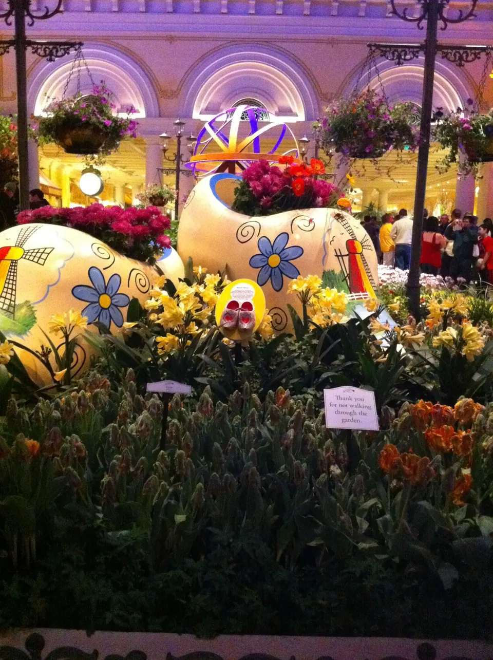 Giant painted Dutch-style eggs with windmills and daisies sit in a bed of daffodils and tulips, with a small sign asking visitors to stay on the path.