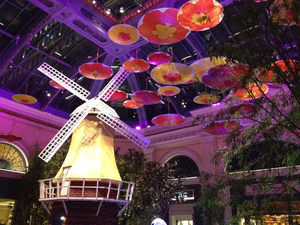 Looking up at a yellow windmill under a glass roof hung with orange and red parasols, lit purple.