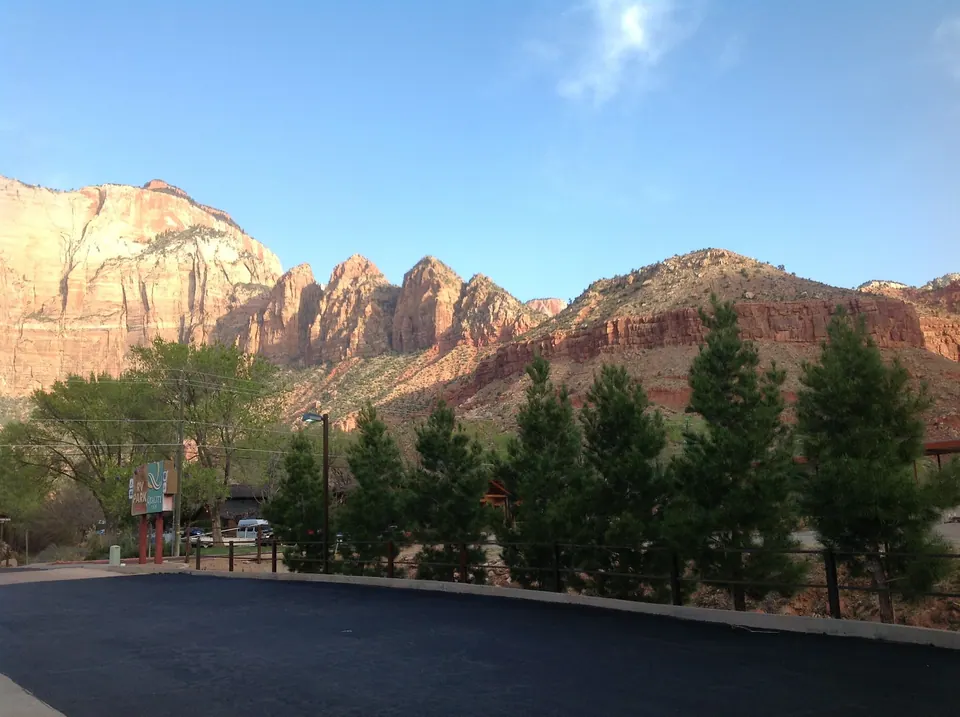 Red rock buttes glow in early sun over a row of evergreens and the motel's green sign at the edge of the lot.