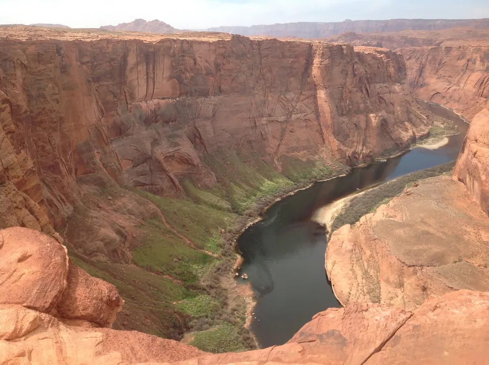 A green river curves around the foot of towering red sandstone cliffs, far below the rocky rim in the foreground.