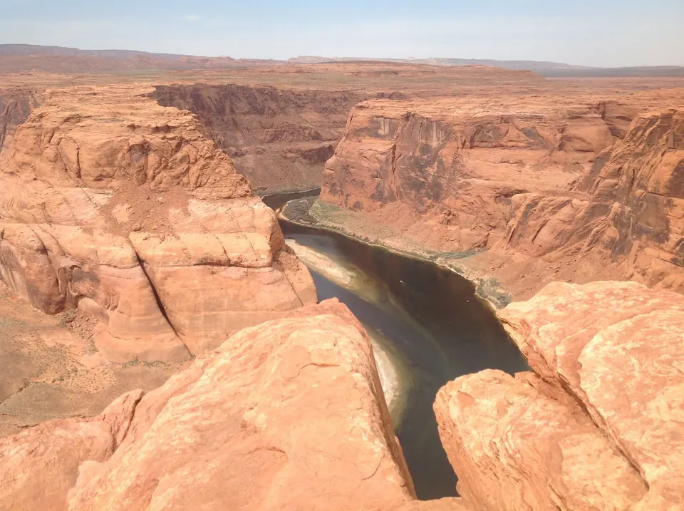 From behind two rocks at the edge, the dark river bends around the base of the sandstone point below.