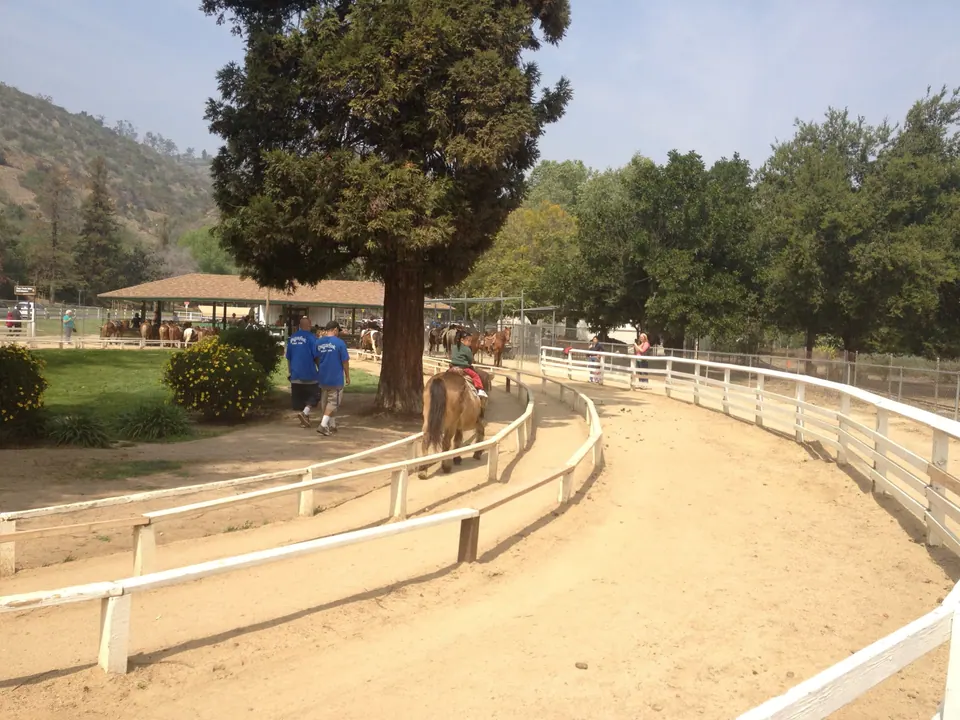 The pony ring at the end of the lap, with two workers in blue shirts walking by, a covered stable area and hills behind.