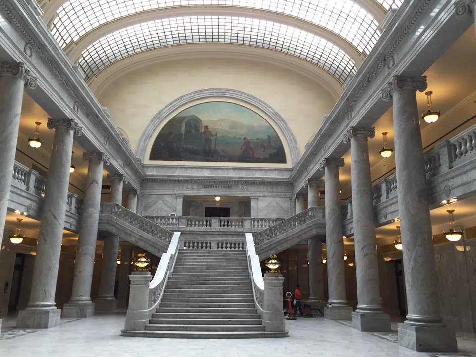 A grand marble staircase rises between tall columns toward a painted arched mural beneath a glass skylight vault.